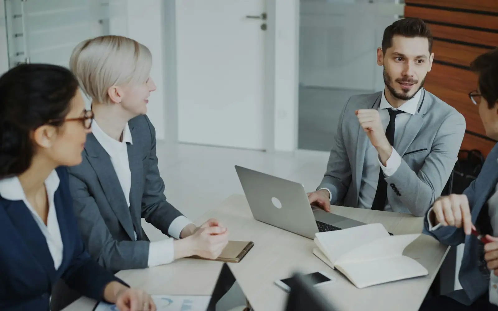 Four professionals in a bright meeting room discussing plans around a laptop and notebooks