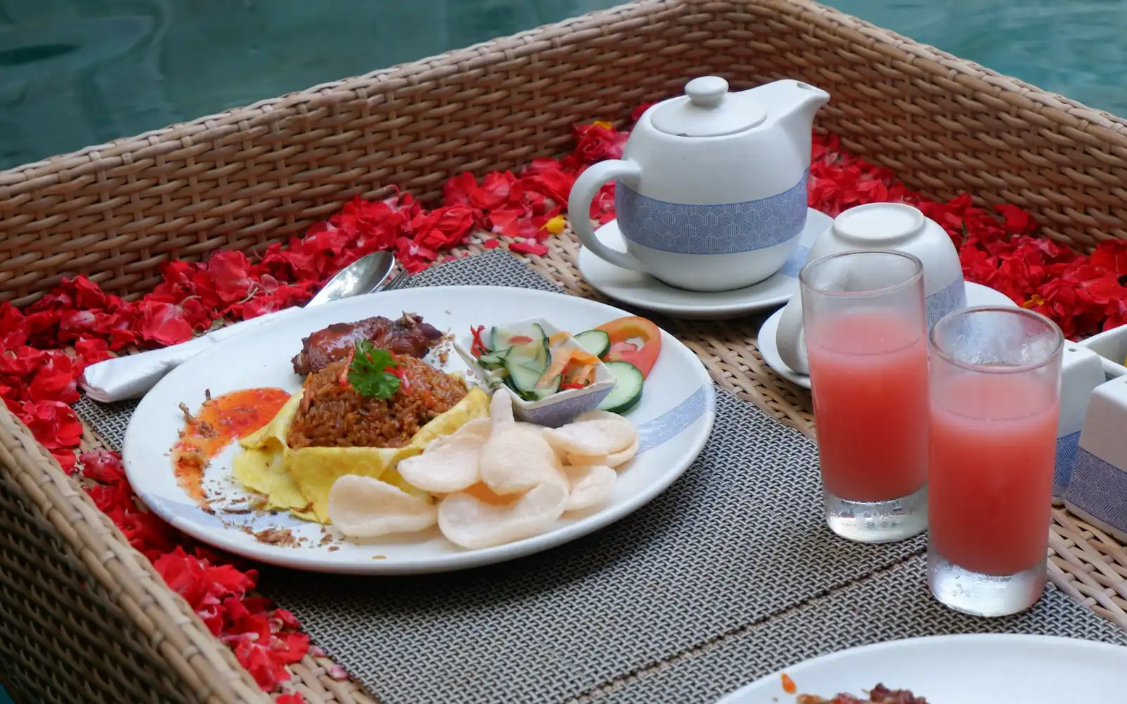 Villa breakfast tray with nasi goreng, prawn crackers, tea and fresh juice on a bed of red petals