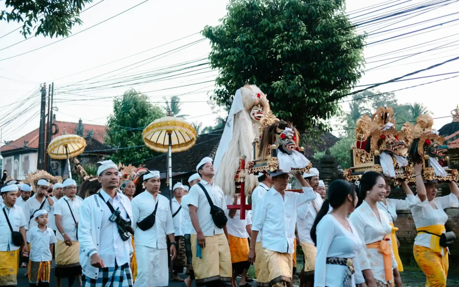 Villagers in white ceremonial dress carrying a Barong and golden parasols in a Balinese temple procession
