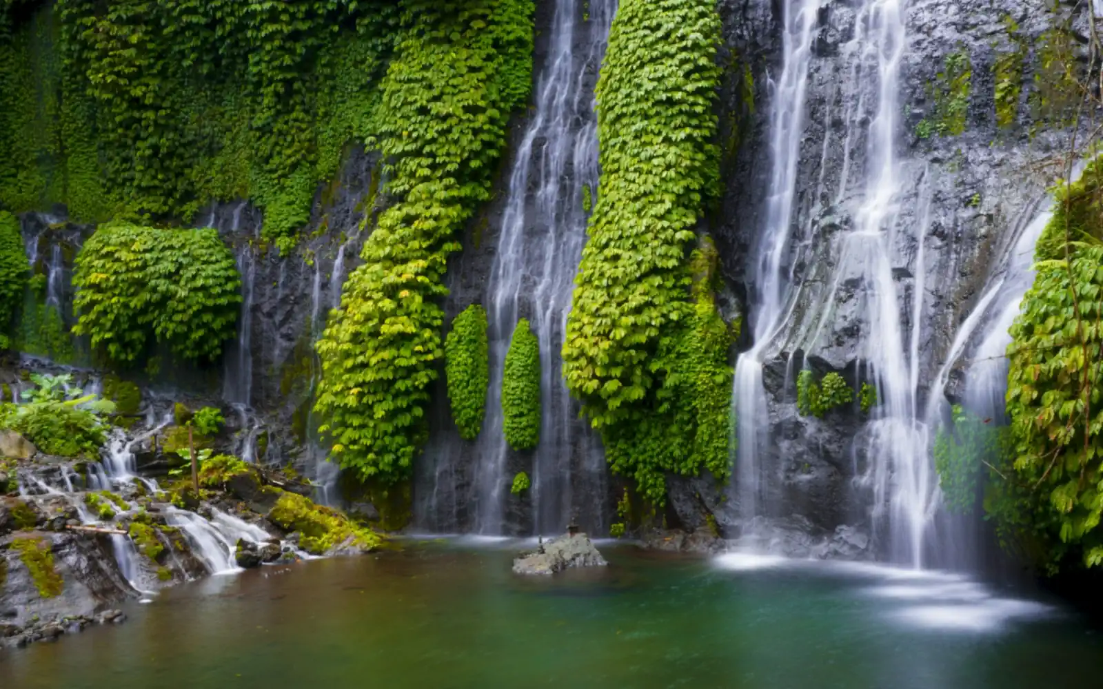 Twin waterfall cascading down moss-covered rock into a green pool in the Bali highlands