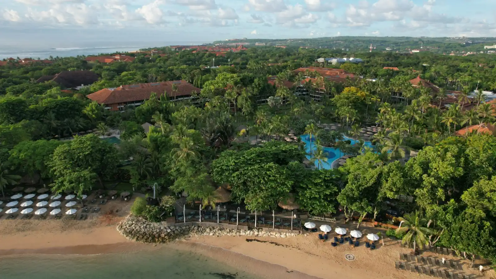 Aerial view of a beachfront resort with tropical gardens, pools and a calm sandy beach in Bali