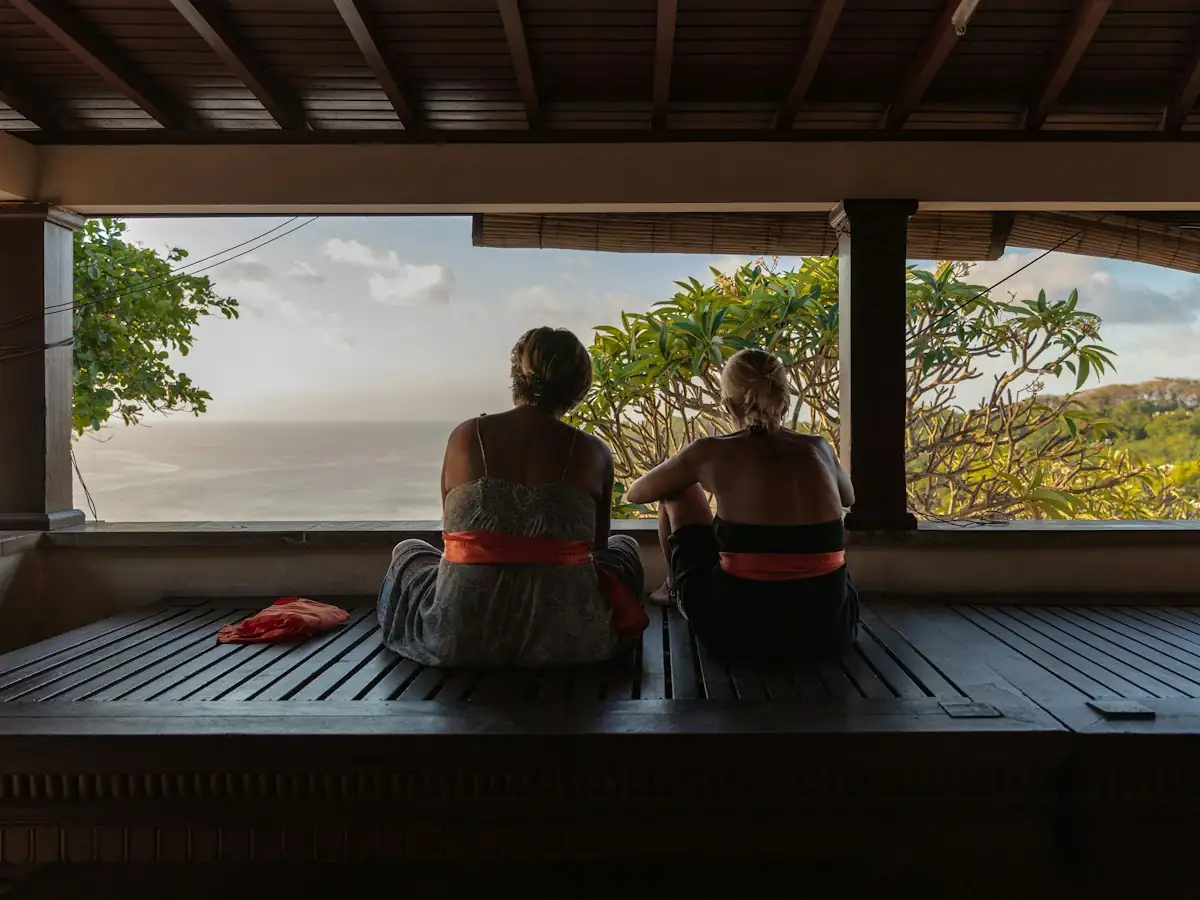 Two people sitting together in a wooden pavilion looking out over frangipani trees toward the sea