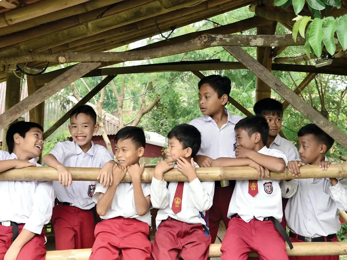 Smiling Indonesian schoolboys in uniforms leaning on the rail of a bamboo pavilion